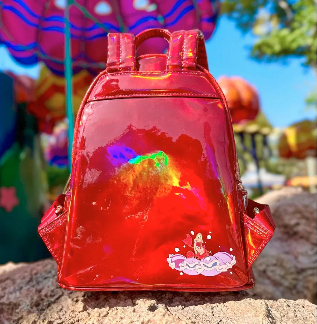 Red reflective backpack with Sebastian playing the clams like drums on a stone surface with colorful background