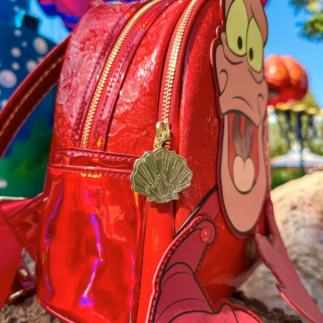 Red metallic backpack with Sebastian's face and claws and shell charm, outdoor background