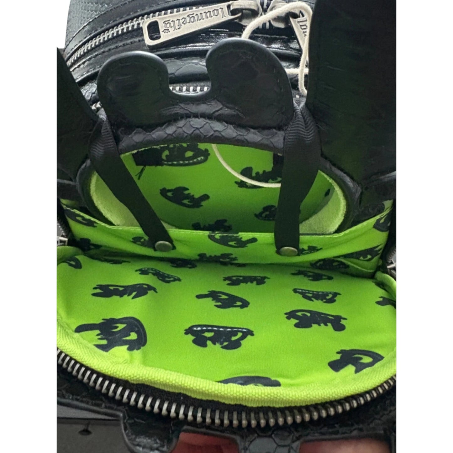 Close-up of a green and black patterned mini backpack ad toothless ears with a zipper.