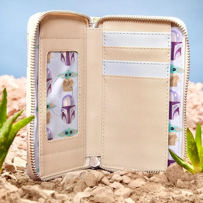 Beige wallet with Mandalorian-themed designs on a rocky surface with plants