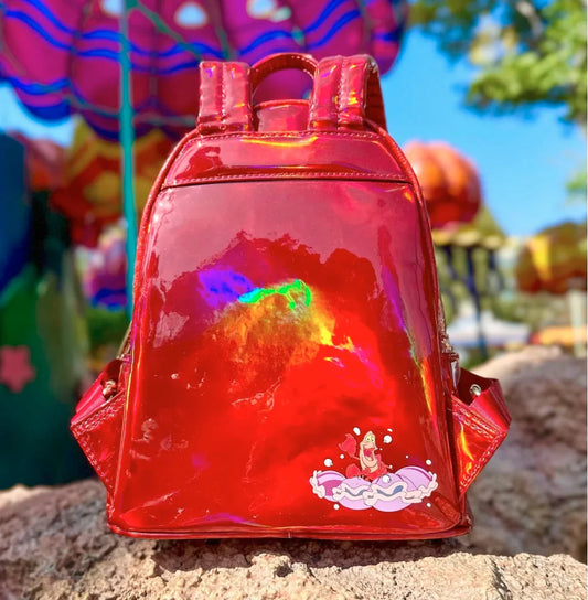 Red reflective backpack with Sebastian playing the clams like drums on a stone surface with colorful background