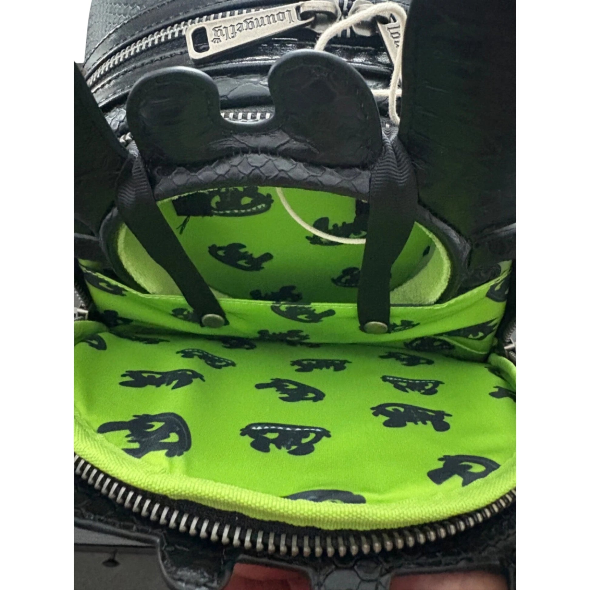Close-up of a green and black patterned mini backpack  ad toothless ears with a zipper.