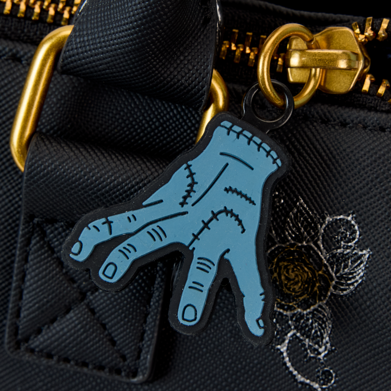 Close-up view of Thing key charm attached to a black Crossbody bag with gold zipper.
